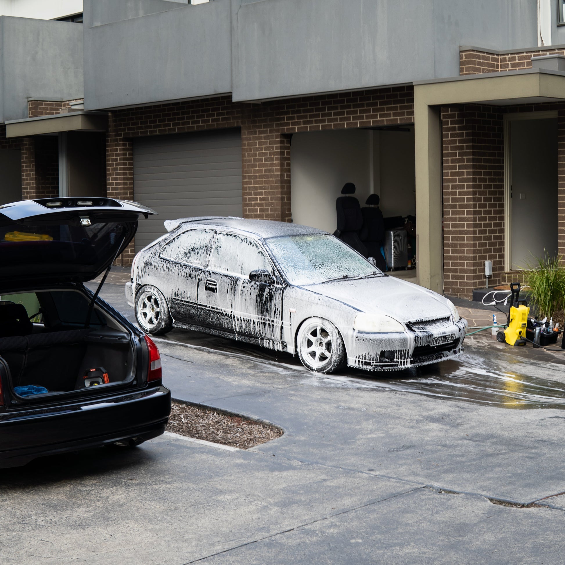 Two cars, one black and one white with black spots, parked in a driveway.